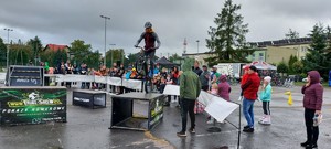 Mężczyzna na rowerze na jednym kole wykonuje pokaz. Wokół grupa dzieci i osób dorosłych.