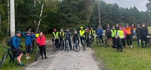 Grupa dorosłych osób na drodze leśnej. Przy nich rowery.
