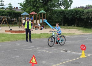 Boisko szkolne. Policjant i dziecko jadące rowerem.