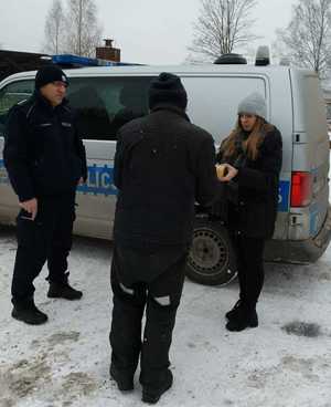 Policjant z pracownikami socjalnymi rozdają ciepłe posiłki potrzebującym.