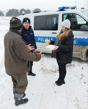 Policjant z pracownikami socjalnymi rozdają ciepłe posiłki potrzebującym.