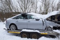 Na zdjęciu srebrny pojazd uszkodzony i zasypany śniegiem stojący na lawecie.