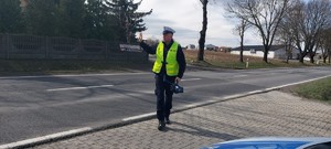 Przy jezdni umundurowany policjant ruchu drogowego prawą  ręką wydaje znak do zatrzymania pojazdu.