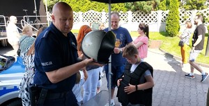 Policjant trzyma w ręku kask, obok dzieci.