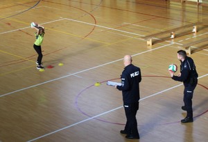 Na hali sportowej dwóch policjantów i dziewczynka rzucająca piłką.