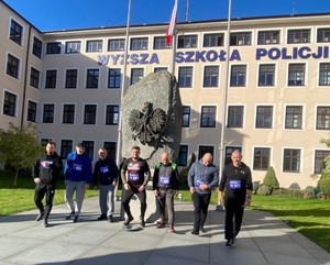 Przed budynkiem Wyższej Szkoły Policji w Szczytnie przy pomniku grupa mężczyzn.
