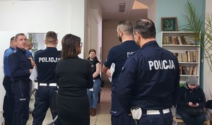 Grupa policjantów i kilka osób oczekujących w poczekalni.