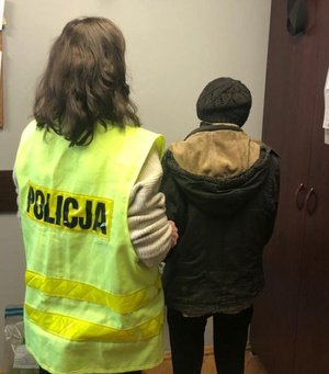 policjantka stoi tyłem w kamizelce odblaskowej z napisem policja obok stoi zatrzymana kobieta