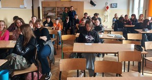 W klasie szkolnej grupa dzieci, z którymi policjantka w towarzystwie kobiety pozują do zdjęcia.