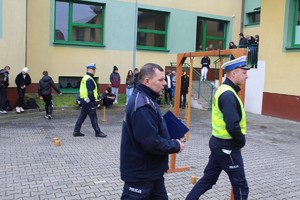 Trzech idących policjantów na placu zewnętrznym szkoły.