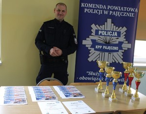 Policjant w sali szkolnej stojący przed stolikiem.