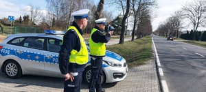 Dwóch policjantów. Jeden z nich mierzy prędkość.