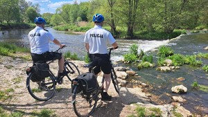 Policjanci na rowerach przy zbiorniku wodnym.