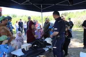 Policjant z dzieciakami pod namiotem, w plenerze. W oddali radiowóz.