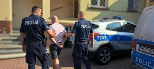 Dwóch umundurowanych policjantów prowadzą zatrzymanego.