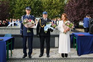 Policjant, strażak, dyrektor szkoły stoją z kwiatami.