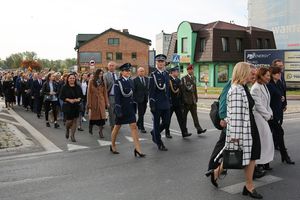 Grupa osób idąca ulicą w szyku. Wśród nich policjantka, policjant, strażak, żołnierz.