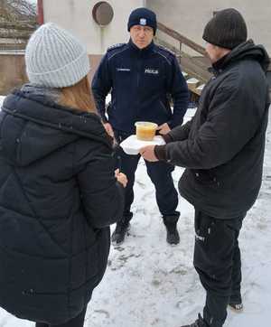 Policjant z pracownikami socjalnymi rozdają ciepłe posiłki potrzebującym.