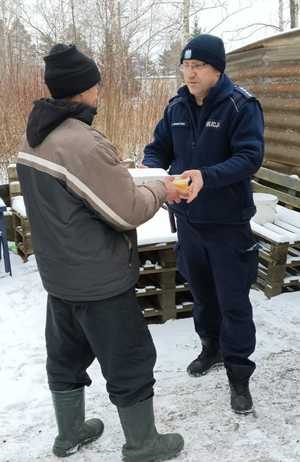 Policjant z pracownikami socjalnymi rozdają ciepłe posiłki potrzebującym.