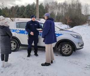 Policjant z pracownikami socjalnymi rozdają ciepłe posiłki potrzebującym.