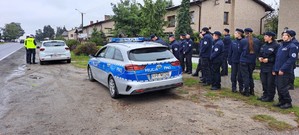 Grupa uczniów przy radiowozie, policjanci kontrolują pojazd.