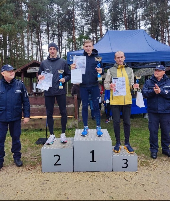 Na podium laureaci. Obok po jednej i drugiej strony podium stoi policjant.