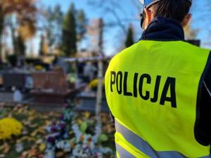 Zdjęcie pleców policjantki. W tle cmentarz.