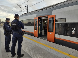 Dwóch umundurowanych policjantów stoi na peronie, na który podjechał pociąg.