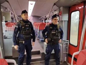 Dwóch umundurowanych policjantów stoi w przedziale pociągu.