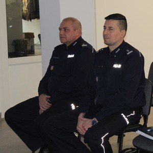 Na krzesłach siedzi dwóch umundurowanych policjantów