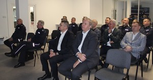 Na zdjęciu widać siedzących na krzesłach umundurowanych policjantów oraz osoby cywilne.