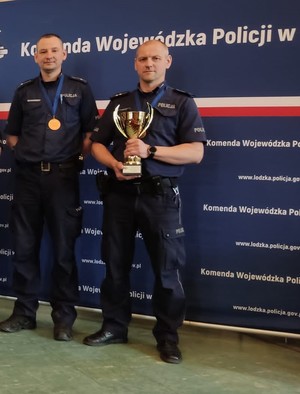 Na zdjęciu 2 policjantów, jeden z nich trzyma puchar.