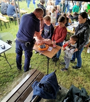 Policjant pokazuje na fantomach masaż serca, przyglądają się temu grupa dzieci.