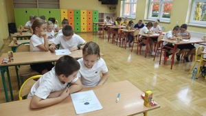 Dzieci siedzą w ławkach.