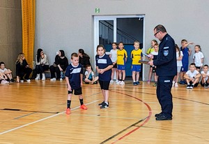 Dzieci ćwiczą na sali, czas mierzy policjant.