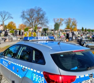 Oznakowany radiowóz, w tle cmentarz.