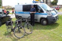 policjant stojący obok radiowozu i dwóch policyjnych rowerów